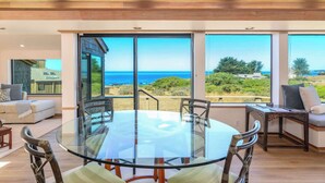 Zona pranzo moderna con tavolo e sedie in vetro, ampie finestre con vista sull'oceano e sul paesaggio.