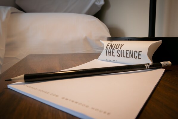 A notepad with a pen on a wooden table, a pillow in the background, and a sign that reads 'ENJOY THE SILENCE'.