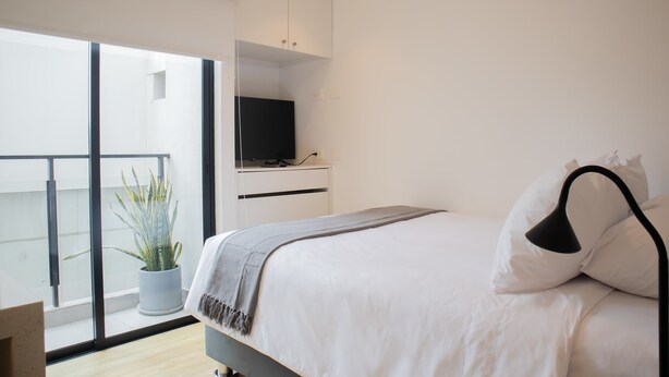 Een moderne slaapkamer met een bed, een tv op een dressoir, een potplant en een balkon met uitzicht.