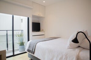 A modern bedroom with a bed, a TV on a stand, a potted plant, and a balcony with a view.