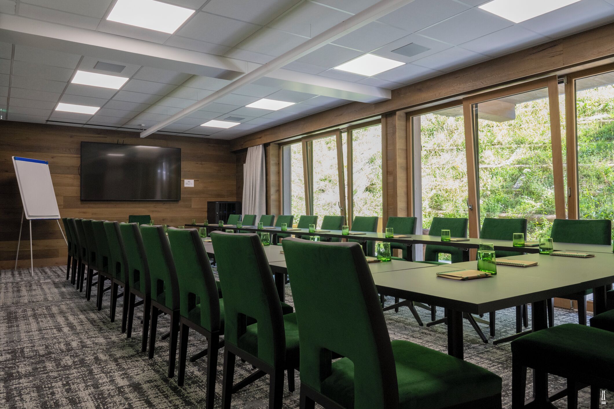 Un salón de conferencias con sillas verdes, una mesa grande, una pizarra y una pantalla de proyector.