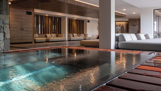 A modern spa area with a heated floor, seating areas, and a stone wall. - Chalet Hôtel le Collet & Spa (Xonrupt-Longemer)