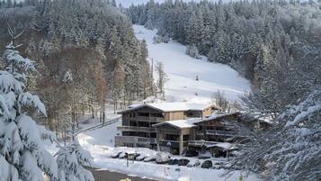 Ein schneegebdecktes Chalet mit mehreren Etagen, einem Parkplatz und einer Skipiste im Hintergrund.