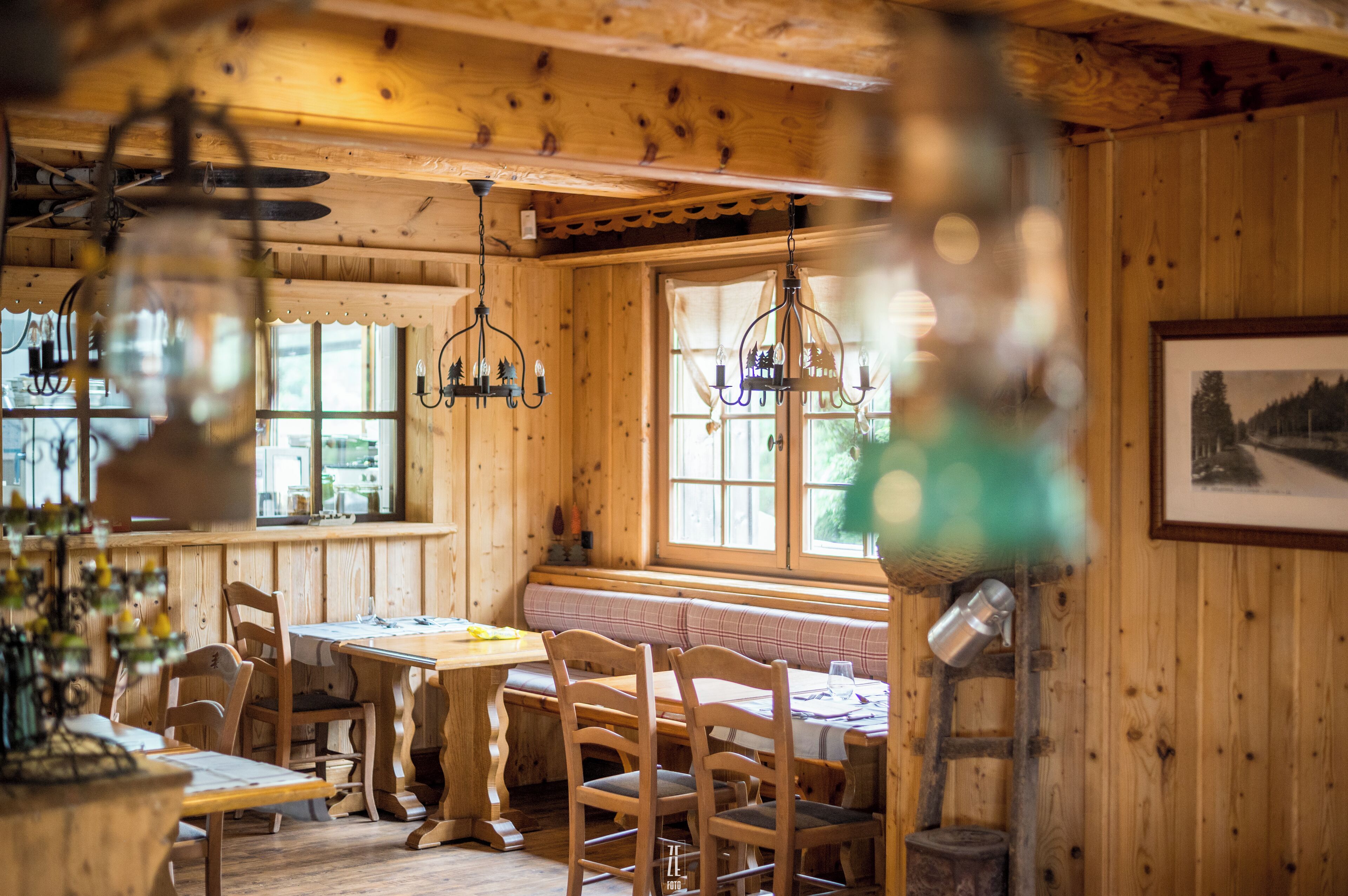 A wooden cabin interior with a dining table, chairs, a bench, and a chandelier.