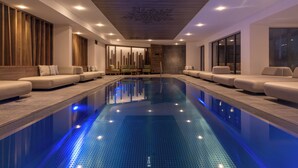 A modern indoor swimming pool with a long, narrow design, surrounded by seating areas and a wooden ceiling. - Chalet Hôtel le Collet & Spa (Xonrupt-Longemer)