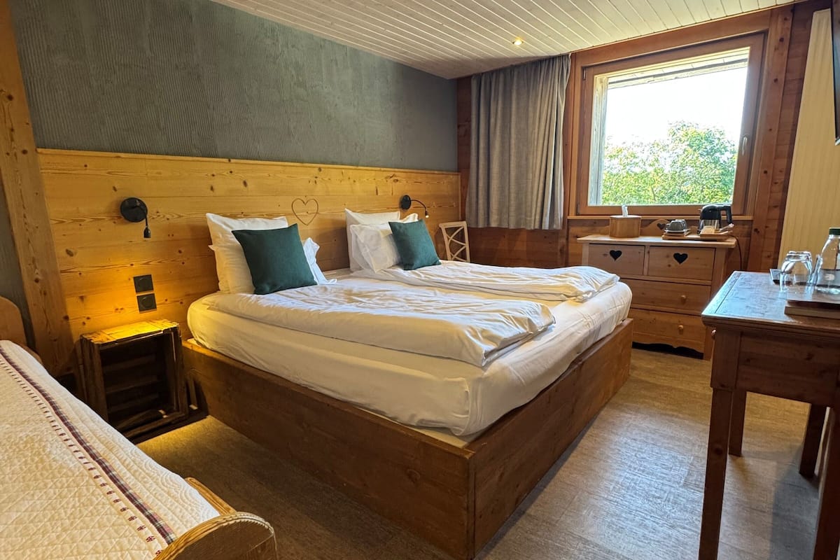 A cozy wooden room with a bed, a small table, and a window with curtains.
