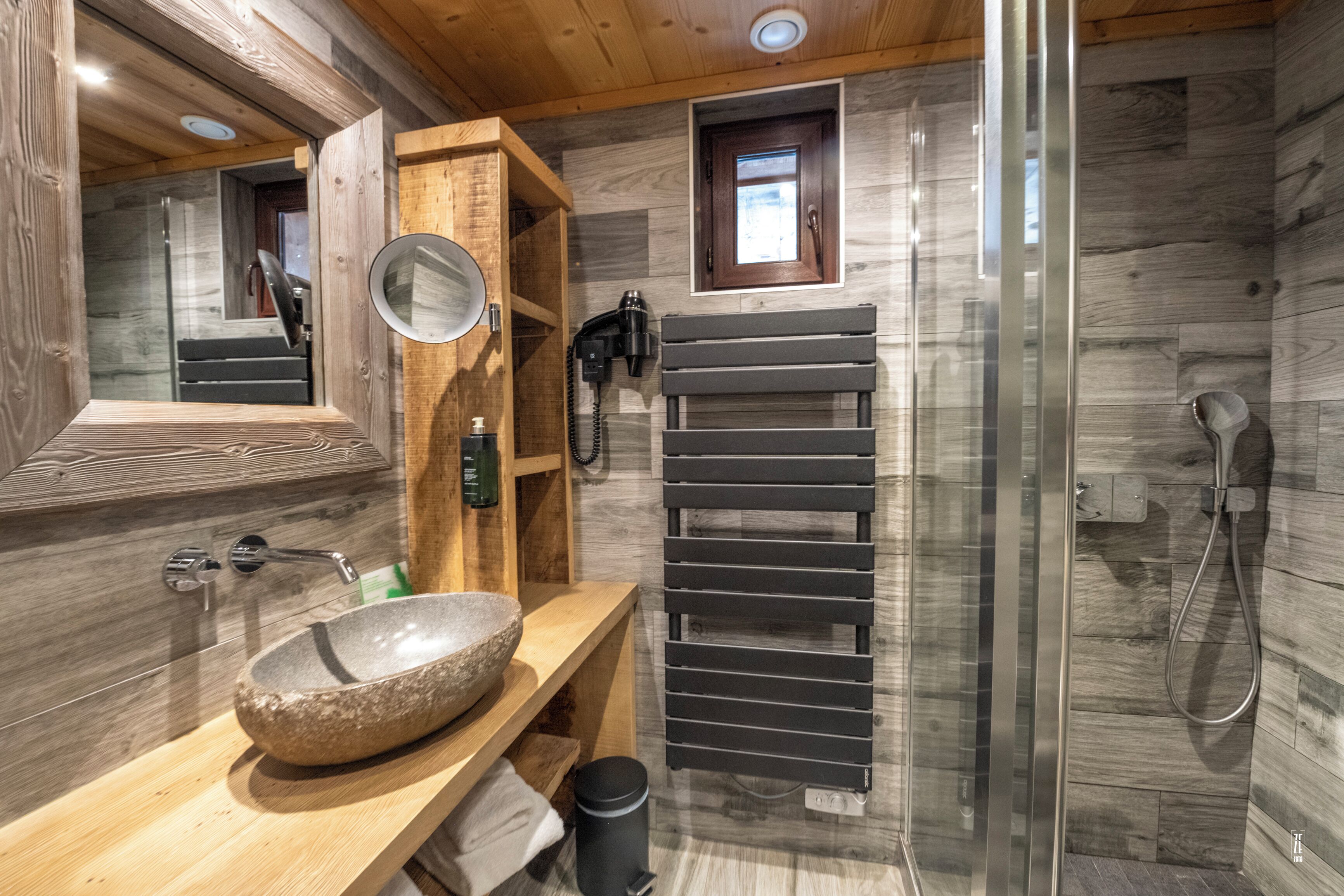 A modern bathroom with a stone sink, wooden vanity, a glass shower enclosure, and a towel rack.