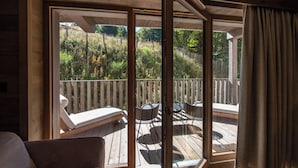 A wooden deck with a glass door leading to a garden. There are lounge chairs and a table on the deck. - Chalet Hôtel le Collet & Spa (Xonrupt-Longemer)