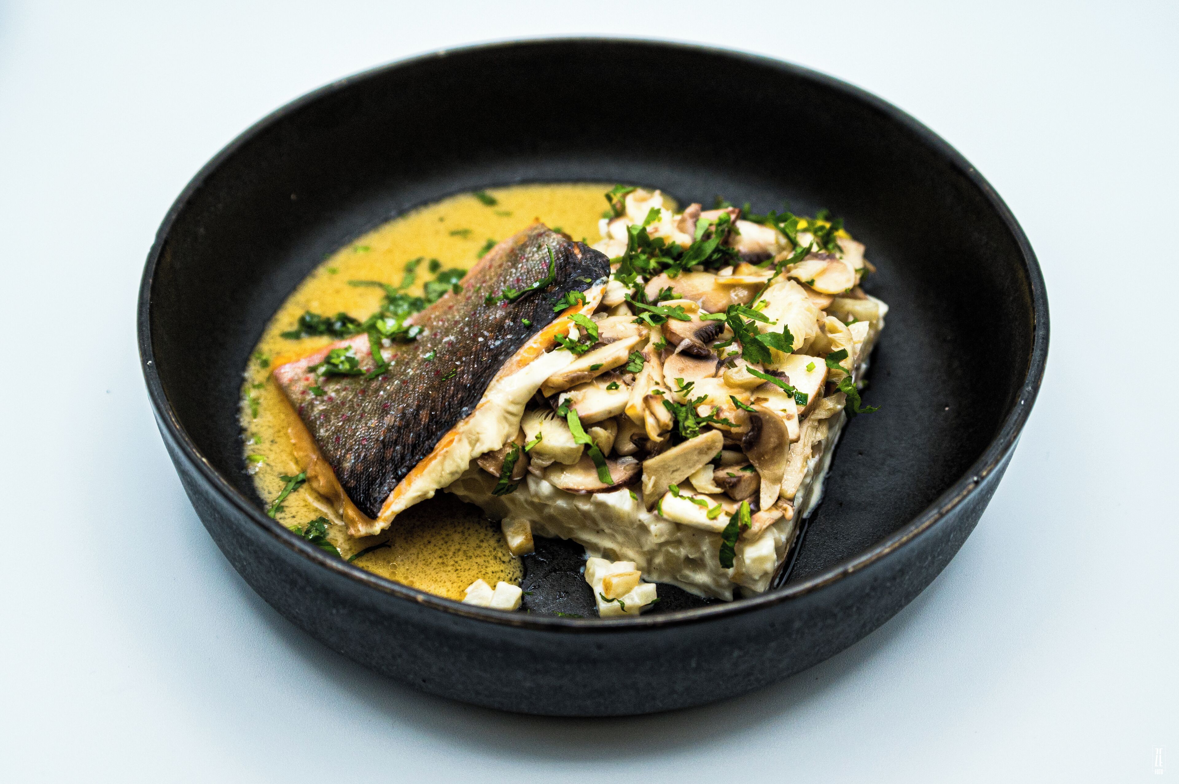 Un plato con pescado y champiñones en un bol negro.