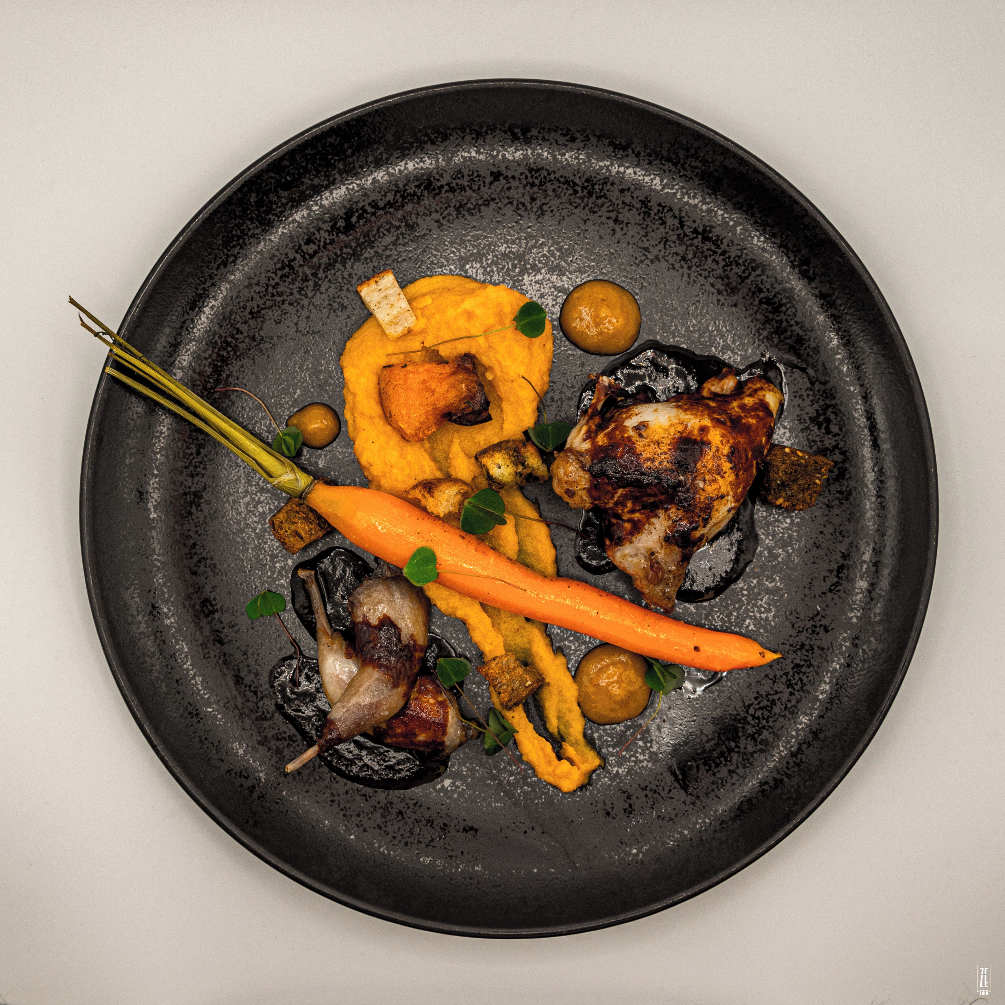 A black plate with roasted chicken, carrots, mushrooms, and a piece of bread.