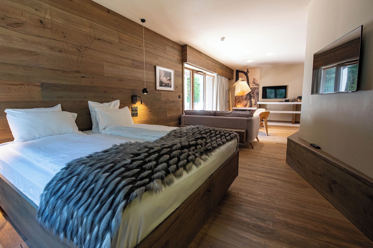 A bedroom with a large bed, a sofa, a TV, and a wooden wall.