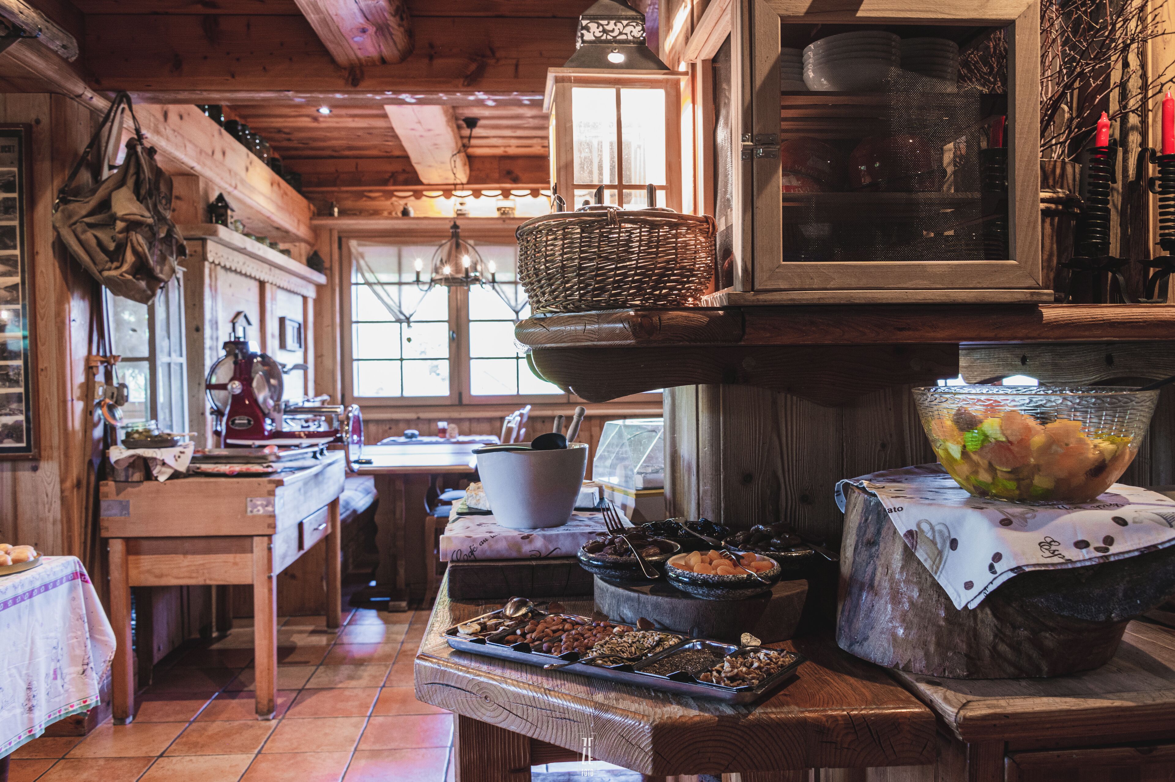 Cocina rústica con vigas de madera, una mesa de madera con diversos alimentos y una ventana que ofrece vistas al exterior.