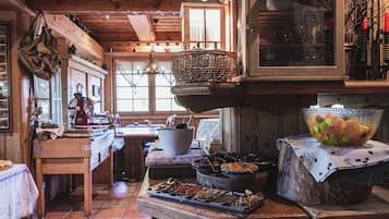 Cocina rústica con vigas de madera, una mesa de madera con diversos alimentos y una ventana que ofrece vistas al exterior.