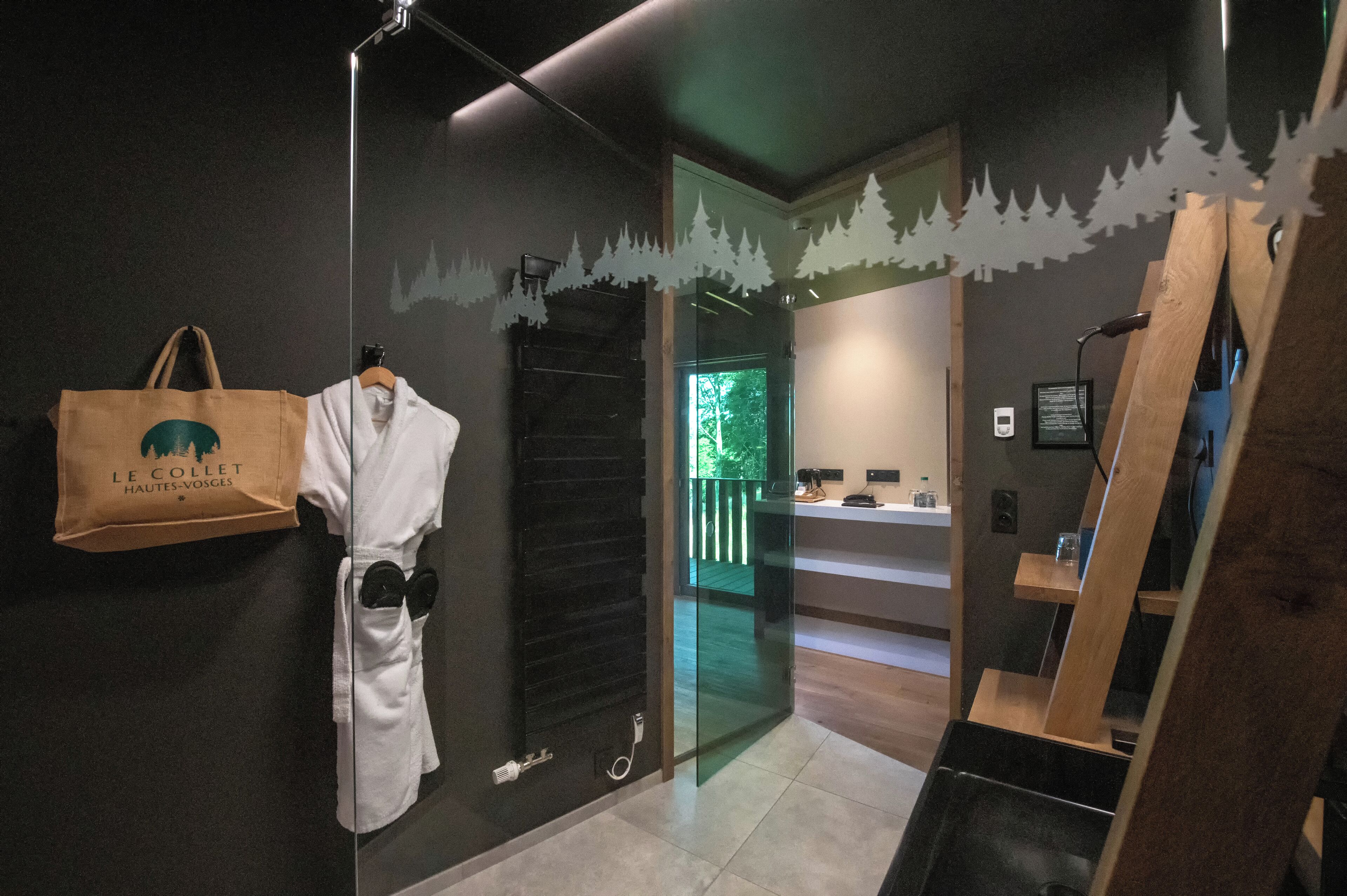 A hotel room with a glass door leading to a balcony, a robe hanging on the wall, and a wooden shelf with items on it.