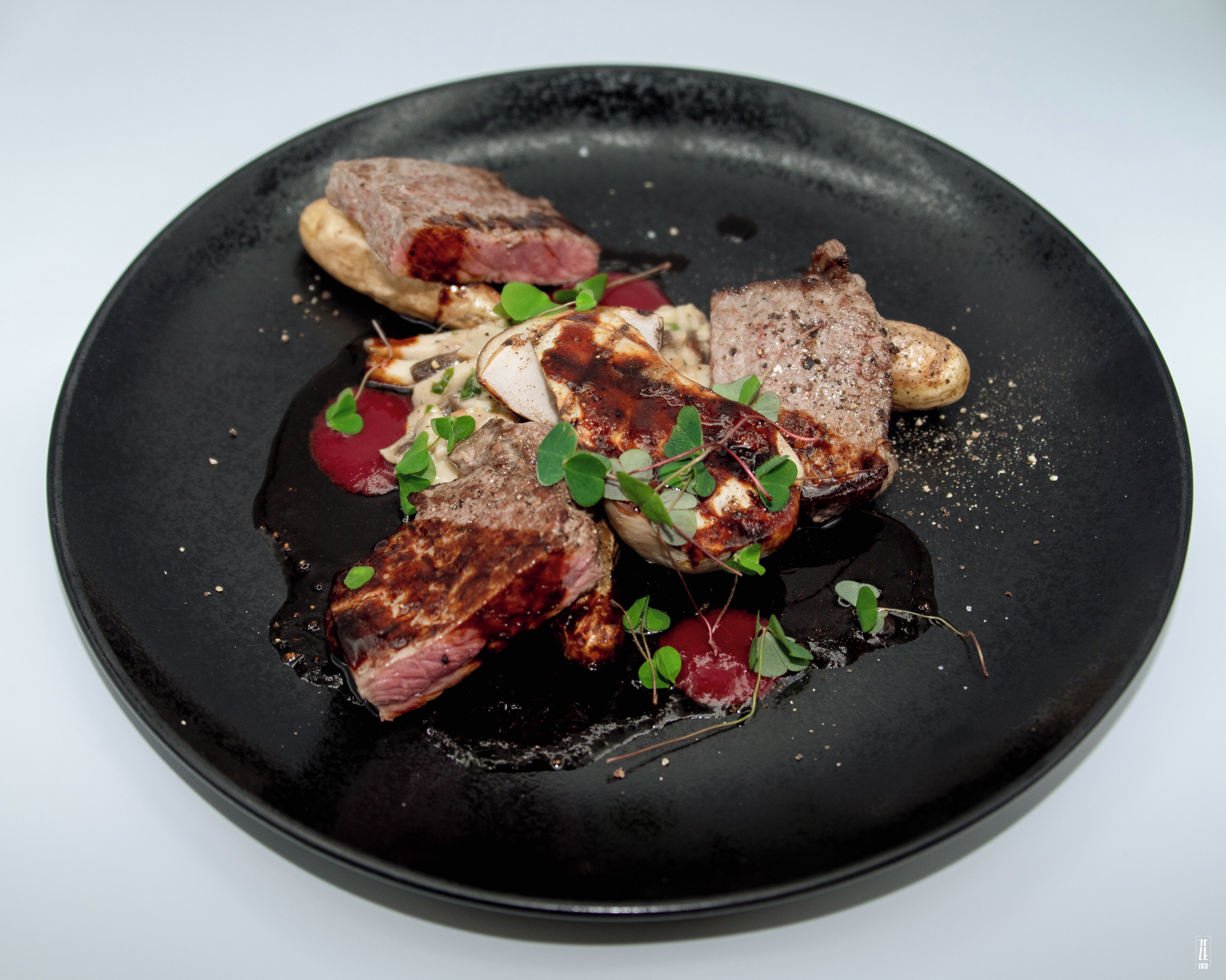 A black plate with grilled meat, mushrooms, and greens.