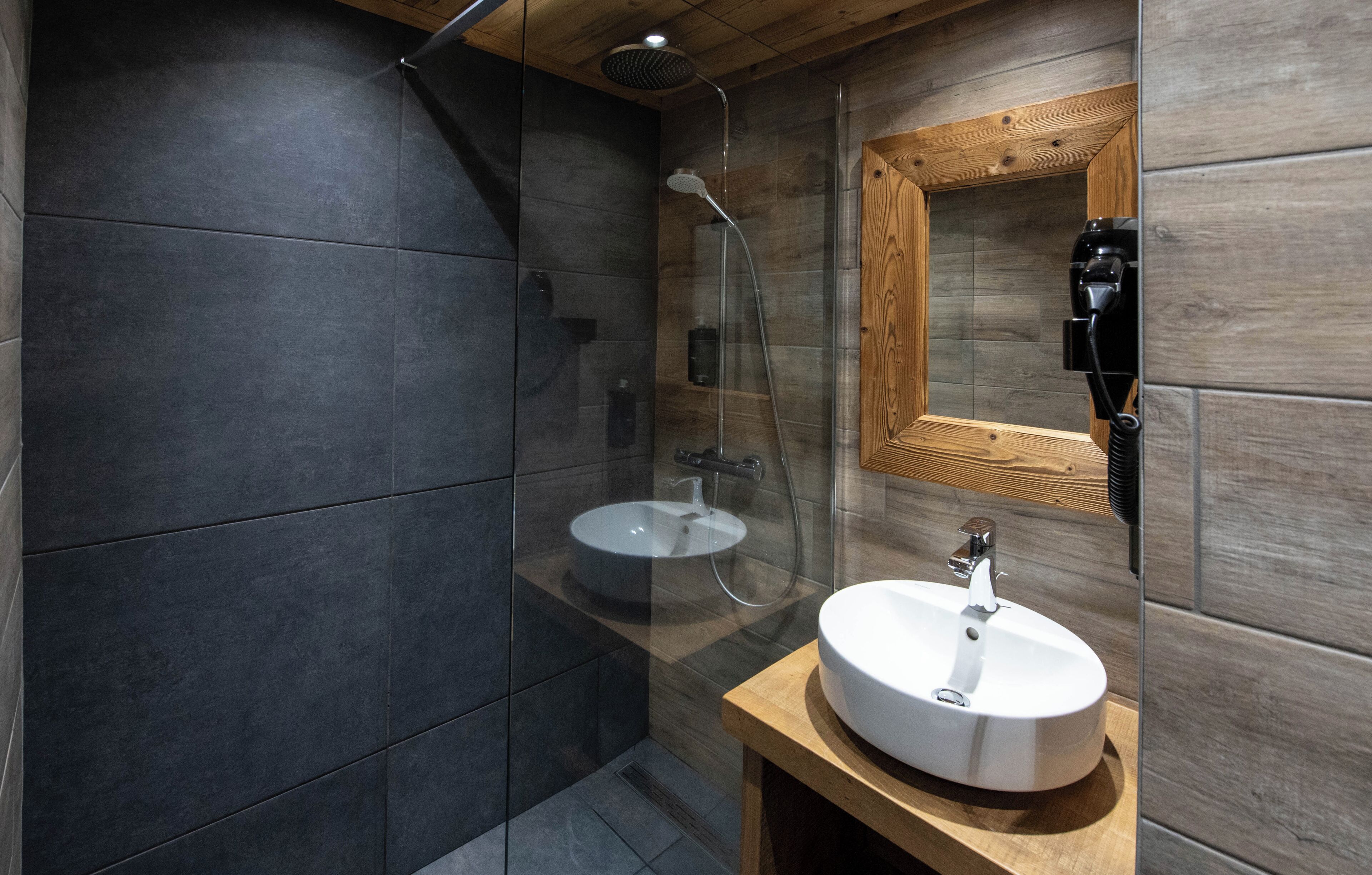 A modern bathroom with a glass-enclosed shower, a wooden vanity with a sink, and a wooden-framed mirror.
