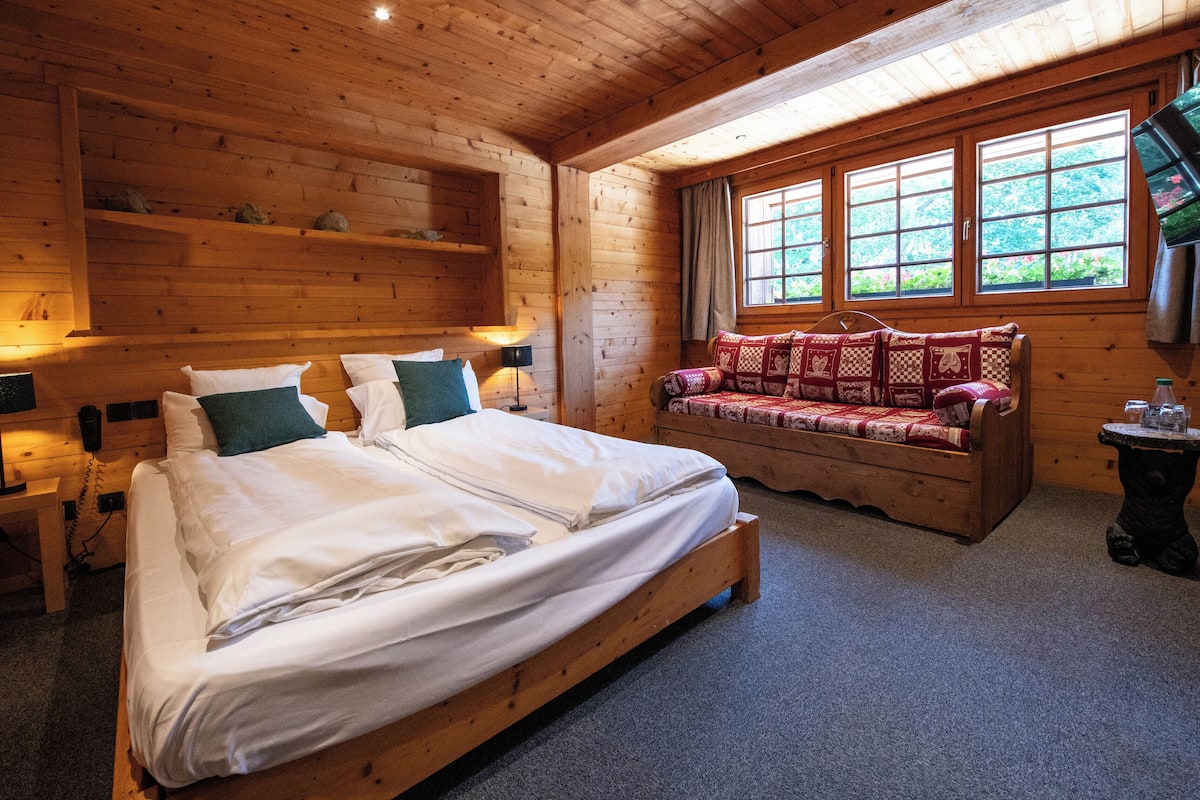 A wooden cabin bedroom with a large bed, a wooden bench, and a television on the wall.