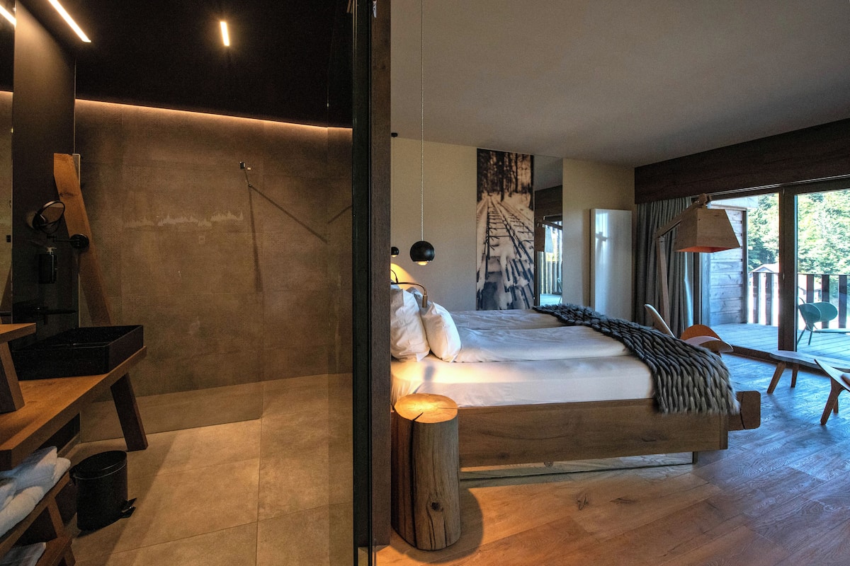 A modern bedroom with a large bed, a wooden bench, and a view of the outdoors.