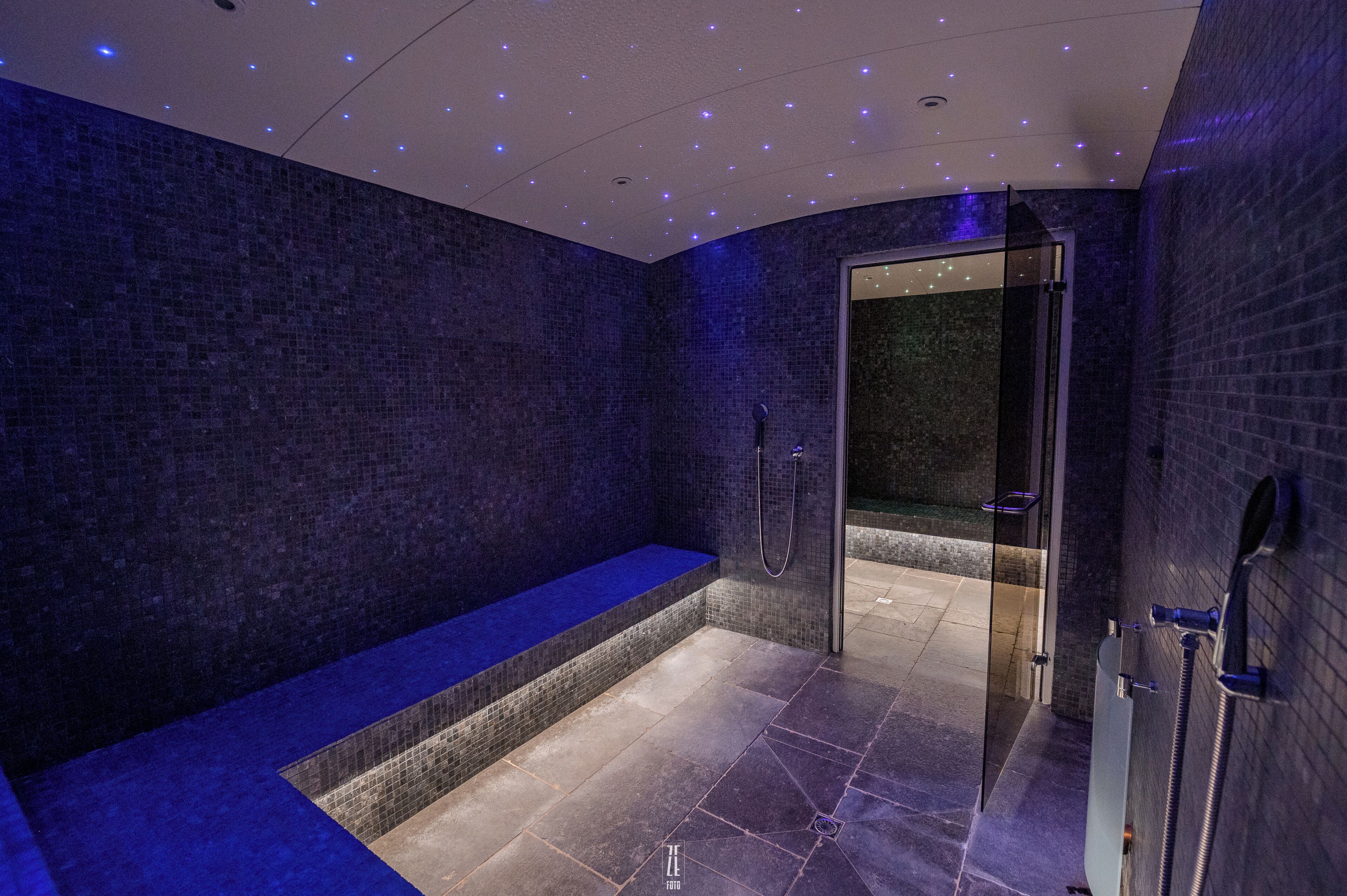 A modern spa room with a blue bench, a glass-enclosed shower area, and a tiled floor.