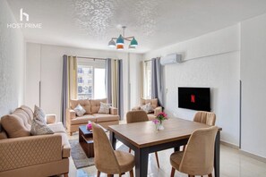 A modern living room with a sofa set, a dining table with chairs, and a flat-screen TV mounted on the wall. - Bright apartment in rehab city  (New Cairo)