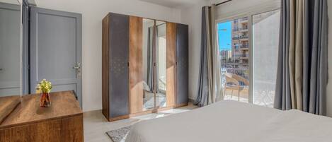 Una habitación de hotel moderna con una cama grande, un armario y un balcón con vistas a la ciudad.