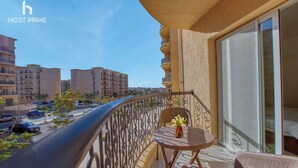 A balcony with a view of the city, a table with chairs, and a vase of flowers.