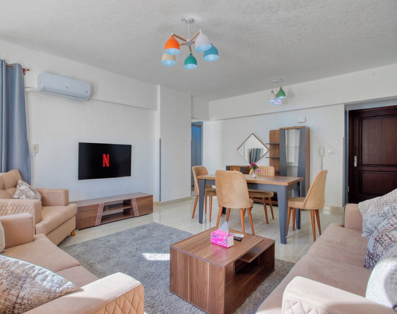 Una sala moderna con televisor de pantalla plana, un comedor con mesa y sillas de madera, y un rincón de estar acogedor con sofás y una mesa de centro.
