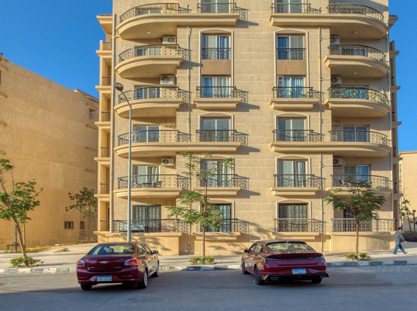 A multi-story hotel with balconies, a clear sky, and two parked cars.