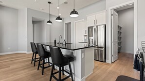 A modern kitchen with a central island, black bar stools, stainless steel appliances, and pendant lighting. - Four Paws & Fairways | Golf Course Front | Pet Friendly | Over $500 in complimentary activities (Mesquite)