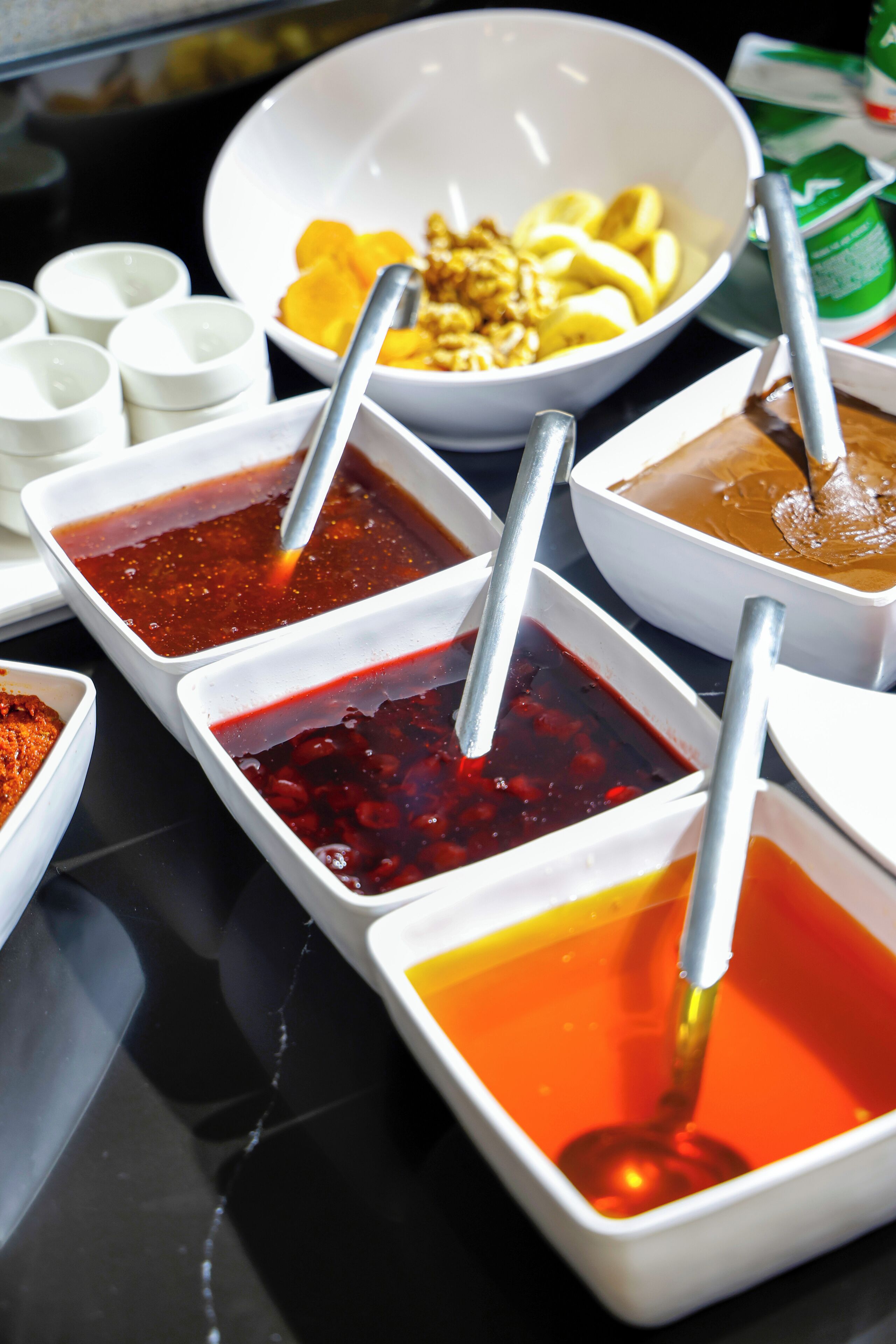 Una mesa con diversos alimentos y condimentos, incluyendo recipientes con diferentes salsas y un bol de fruta.
