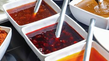 Una mesa con diversos alimentos y condimentos, incluyendo recipientes con diferentes salsas y un bol de fruta.