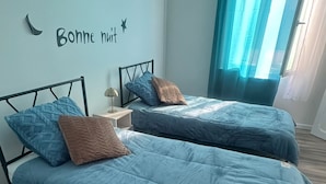A bedroom with two beds, a nightstand, a wall clock, and a window with curtains.