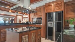 A modern kitchen with wooden cabinets, a stainless steel refrigerator, and a central island. - Zenith Villa | Luxury - 6 Bedroom Villa in Surin with Sea View (Cheong Thale)
