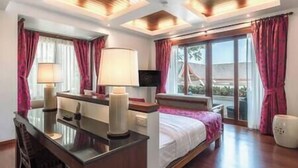 A hotel room with a bed, bedside tables, a desk, a chair, a lamp, a TV, and a window with curtains. - Zenith Villa | Luxury - 6 Bedroom Villa in Surin with Sea View (Cheong Thale)