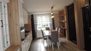 Une cuisine avec des meubles de rangement en bois, une table à manger avec des chaises et une fenêtre avec des rideaux.
