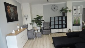Un salon moderne avec un canapé gris, un meuble blanc, un fauteuil gris, une petite table et une grande plante en pot.