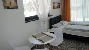 Quarto de hotel com cama, uma pequena mesa com cadeiras, janela com cortinas e obras de arte nas paredes.