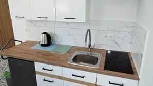 Uma cozinha com armários brancos, uma pia de aço inoxidável, um fogão por indução preto e uma tábua de corte verde.