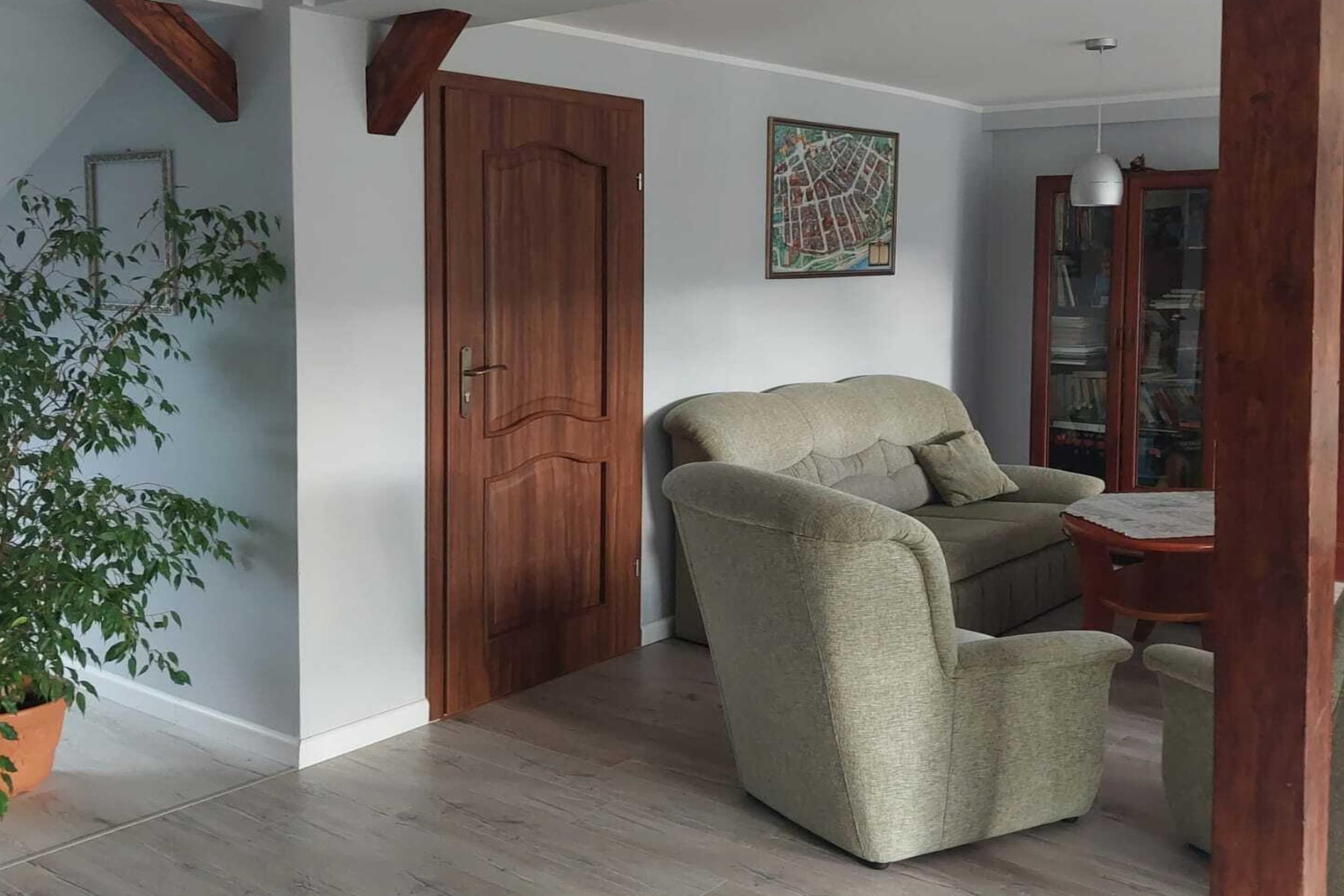 Una habitación con una puerta de madera, un sillón verde, una mesita y una planta en maceta.