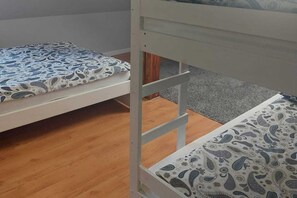 Un lit superposé avec une literie à motifs, un plancher en bois et un tapis gris.