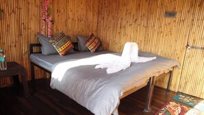 A room with a bed, pillows, a water bottle, and a small table. - Shivadri Resort  (Rishikesh)