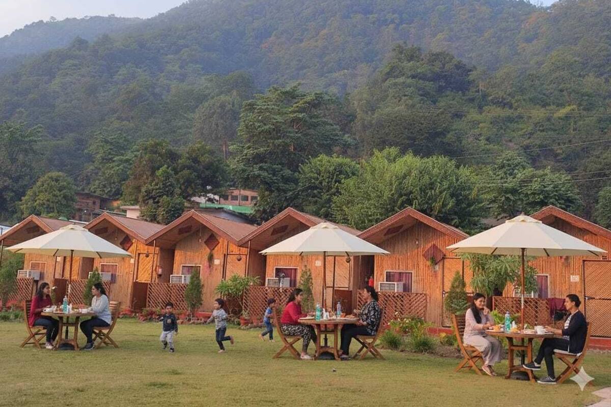 Varias cabañas de madera con áreas de estar al aire libre, rodeadas de exuberante vegetación y colinas.