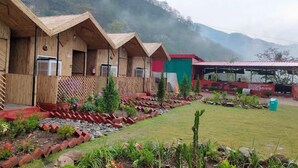 Wooden cabins with external air conditioning units, a garden with various plants, and a mountain backdrop. - Shivadri Resort  (Rishikesh)