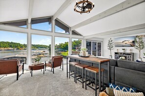 Ein geräumiges Zimmer mit großen Fenstern, die auf einen Fluss blicken, einer Bar und einer Sitzecke mit einer Couch und Sesseln.
