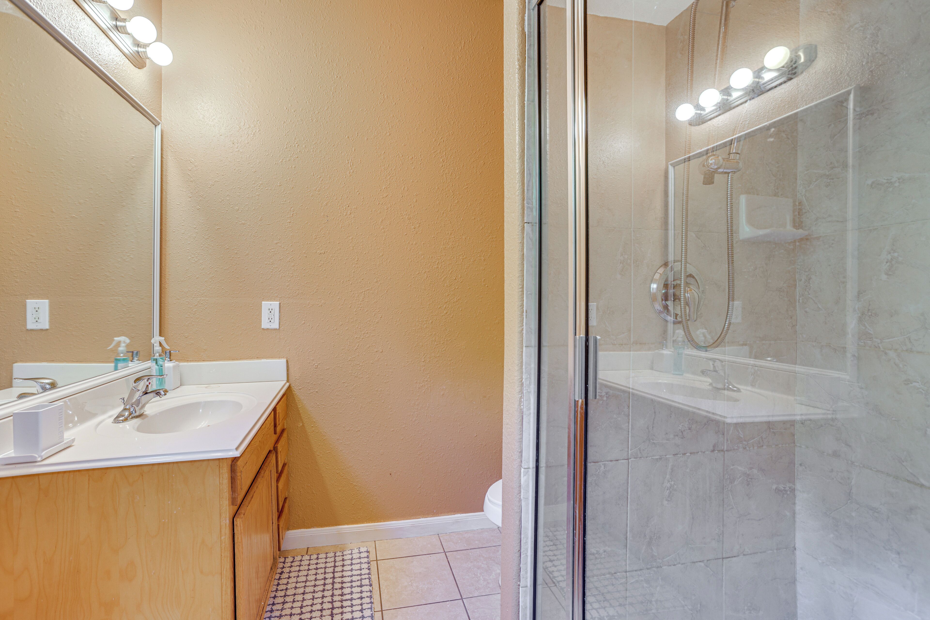 A bathroom with a glass shower enclosure, a sink with a mirror, and a vanity with cabinets.