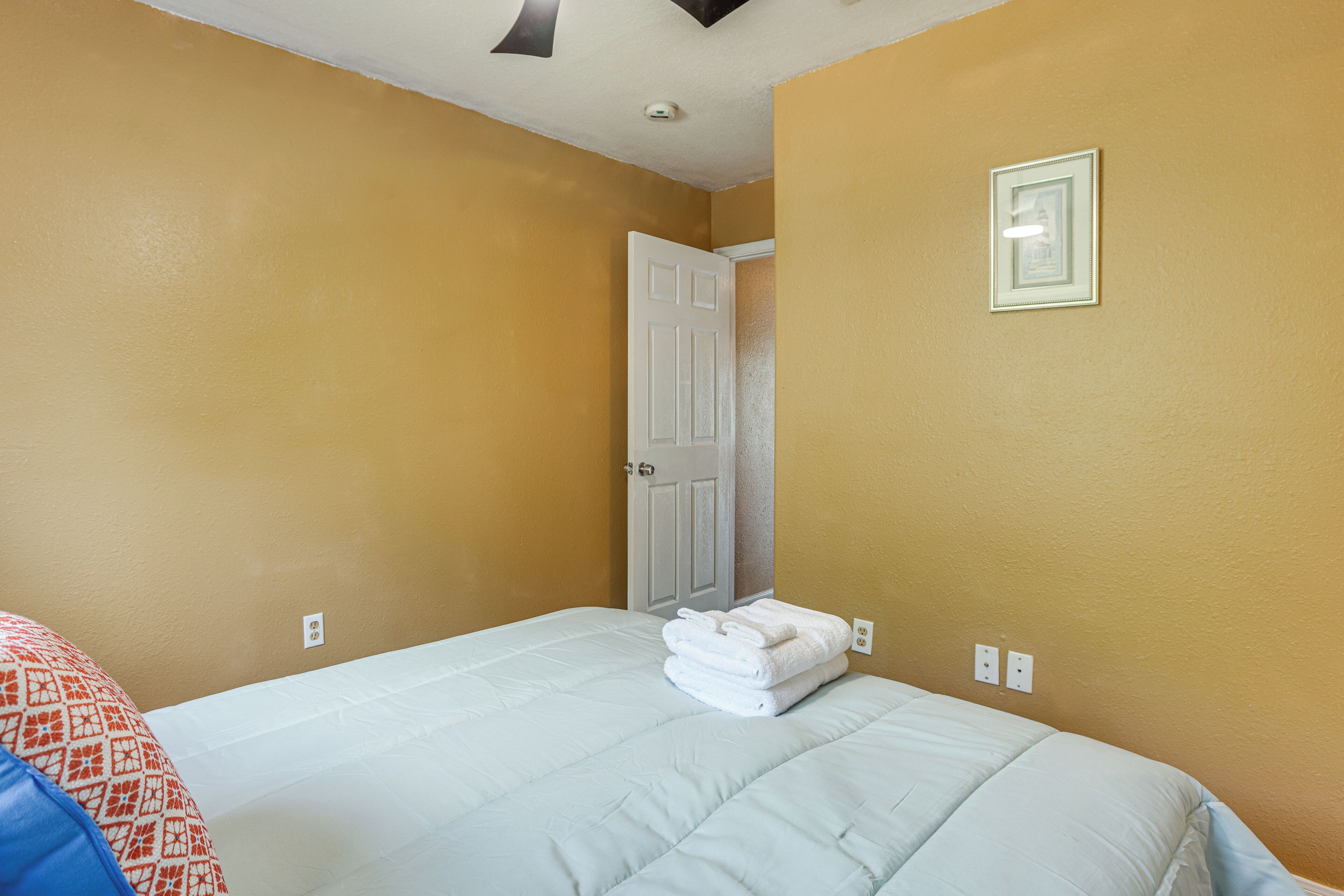 A hotel room with a bed, a door, and a wall-mounted light fixture.