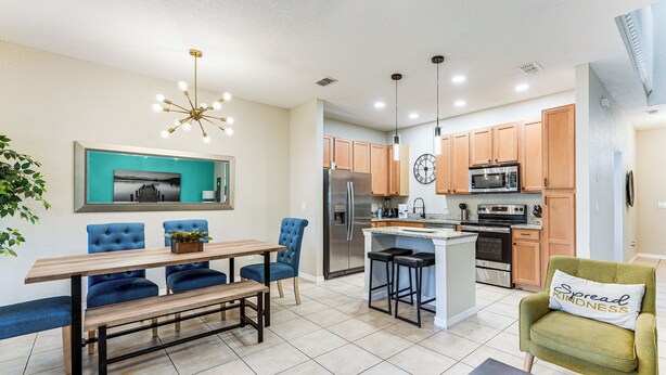 A modern kitchen with wooden cabinets, a stainless steel refrigerator, and a central island with bar stools. - Resort Amenities, Screened Lanai: Kissimmee Escape (Kissimmee)