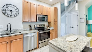 A modern kitchen with wooden cabinets, stainless steel appliances, a granite countertop, and a wall clock. - Resort Amenities, Screened Lanai: Kissimmee Escape (Kissimmee)