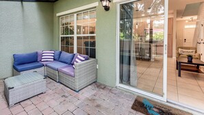 A covered patio area with a wicker sofa, a small table, and a wicker basket. - Resort Amenities, Screened Lanai: Kissimmee Escape (Kissimmee)