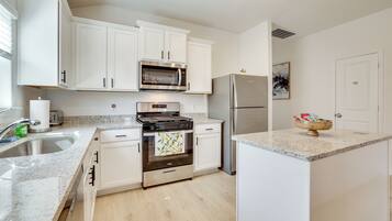A modern kitchen with white cabinets, stainless steel appliances, a granite countertop, and a small island.